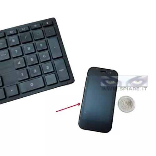 Mini Cellulare Spia con GPS e Registrazione Remota accanto a tastiera e moneta - Dimensioni reali ultra compatte per massima discrezione.