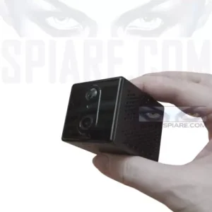 piccola telecamera 4g spia nera a forma di cubo con doppie lenti, tenuta tra il pollice e l'indice. Sull'immagine è presente il testo filigranato 'SPIARE.COM'