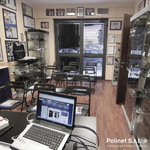 Postazione docente e area didattica nell'aula formazione Polinet Roma, con monitor, strumentazione TSCM professionale, sedie con materiale didattico e certificazioni CCIAA alle pareti