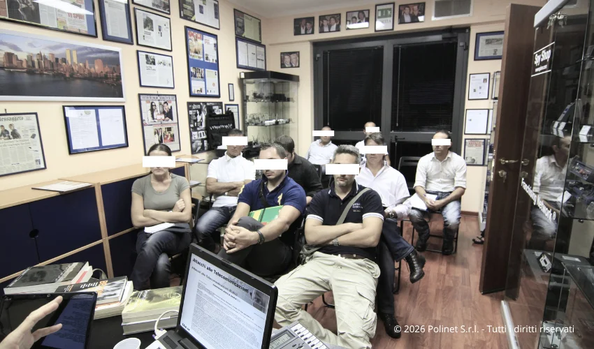 Gruppo di investigatori privati e operatori delle Forze dell'Ordine durante il corso pratico di bonifica ambientale e TSCM di Polinet S.r.l. a Roma. I volti sono oscurati per garantire la massima riservatezza dei partecipanti. Sullo sfondo si notano le pareti dell'aula allestite con certificazioni, riconoscimenti e rassegna stampa dell'azienda.